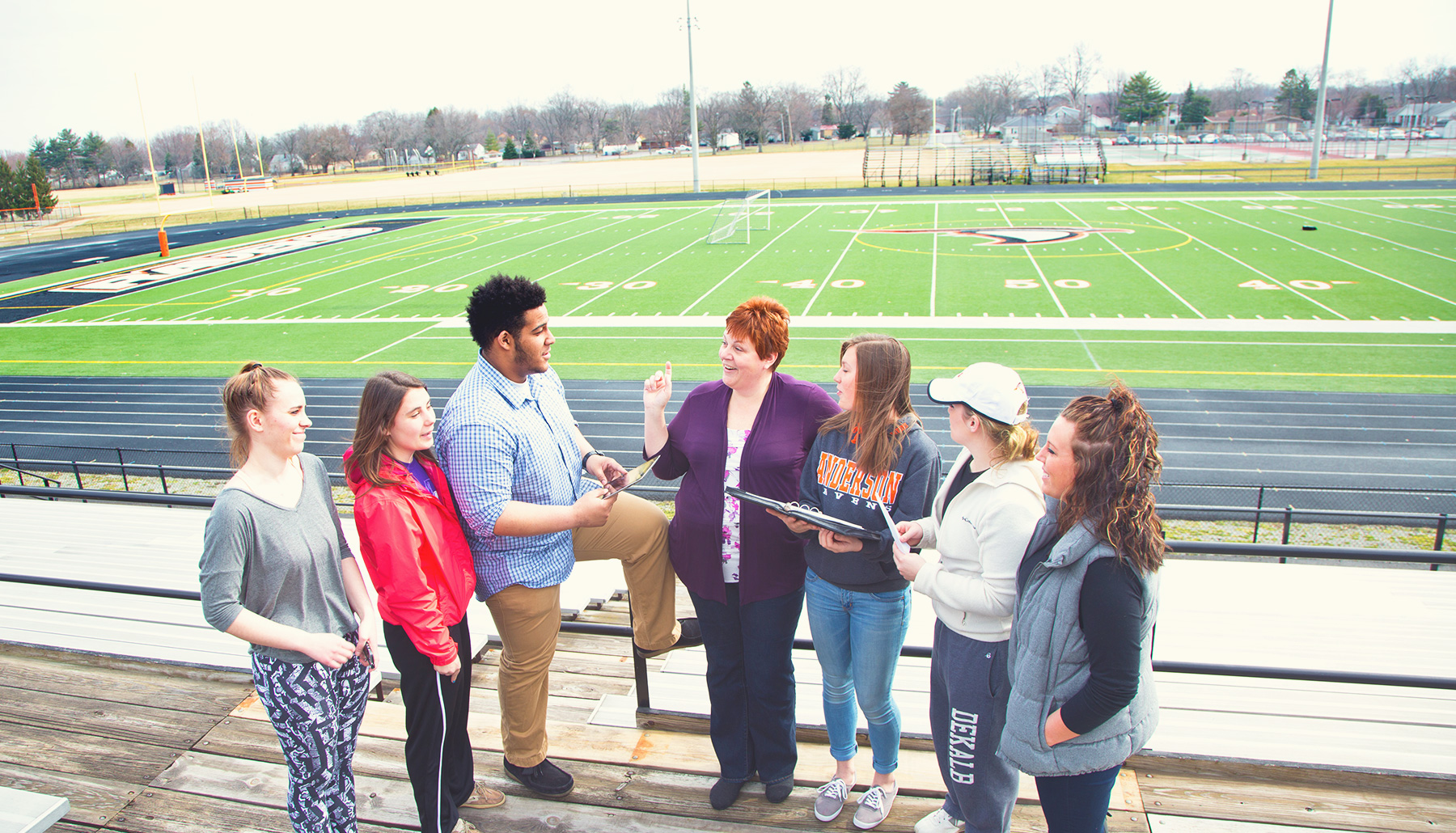 a female professor talks to six students at the football field