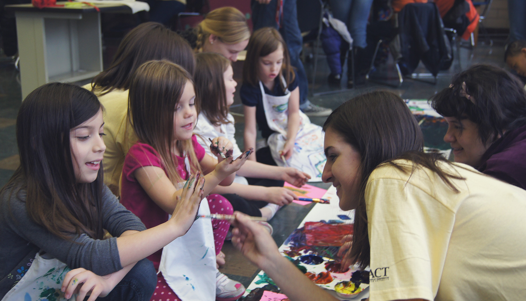 young woman paints the hands of children for an art project